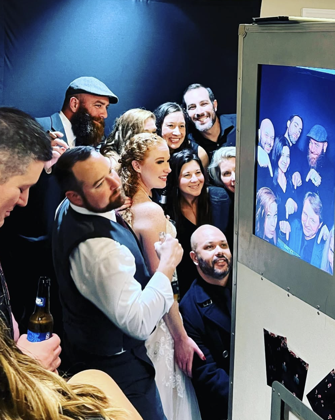 Wedding party crowded around the photo booth screen at a reception